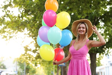 Photo of Portrait of smiling woman in hat and dress with bunch of colorful balloons outdoors