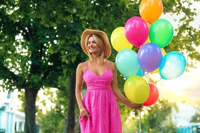 Photo of Smiling woman in hat and dress with bunch of colorful balloons outdoors, low angle view