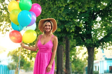 Photo of Portrait of smiling woman in hat and dress with bunch of colorful balloons outdoors. Space for text