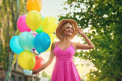 Photo of Smiling woman in hat and dress with bunch of colorful balloons outdoors, low angle view