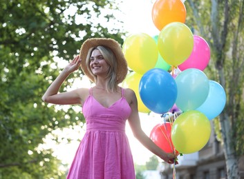 Photo of Smiling woman in hat and dress with bunch of colorful balloons outdoors, low angle view
