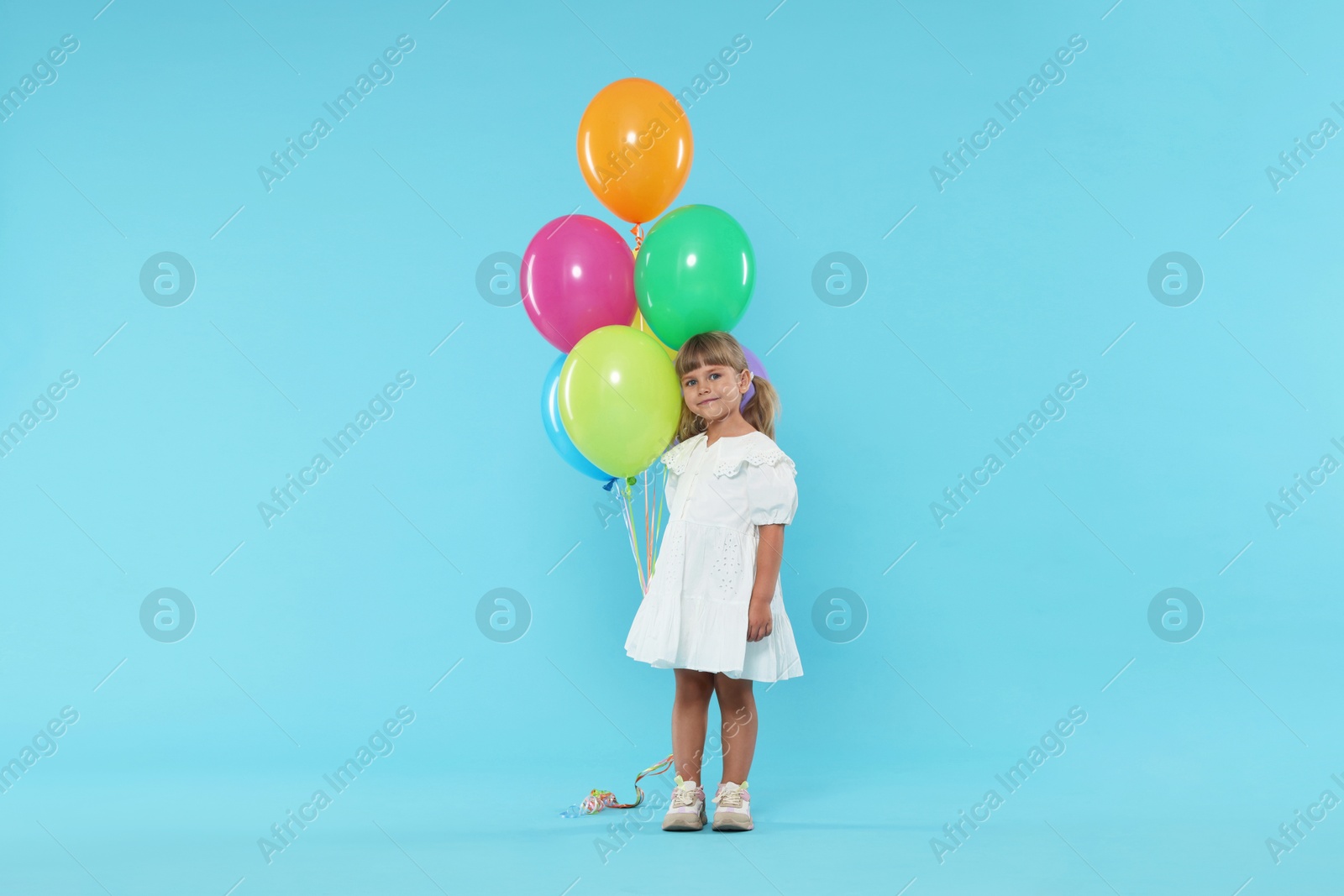 Photo of Cute little girl in dress with bunch of colorful balloons on light blue background