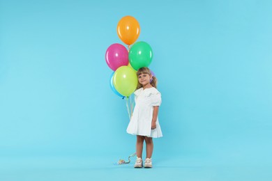 Photo of Cute little girl in dress with bunch of colorful balloons on light blue background