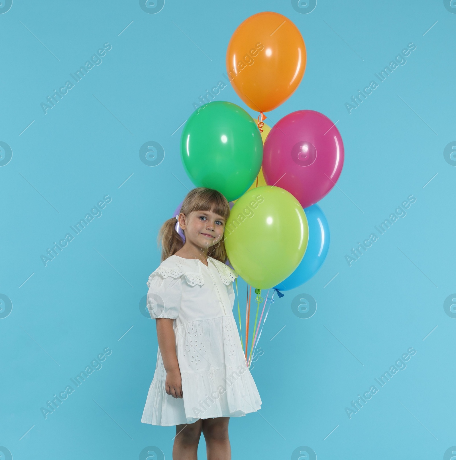 Photo of Cute little girl in dress with bunch of colorful balloons on light blue background