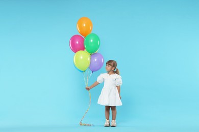 Photo of Cute little girl in dress with bunch of colorful balloons on light blue background