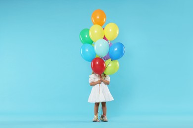 Photo of Little girl in dress hiding behind bunch of colorful balloons on light blue background