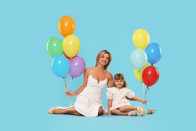 Photo of Happy mother and her little daughter with bunches of colorful balloons on light blue background