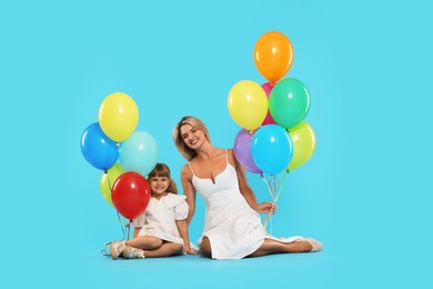 Photo of Happy mother and her little daughter with bunches of colorful balloons on light blue background
