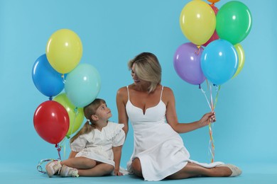 Photo of Happy mother and her little daughter with bunches of colorful balloons on light blue background