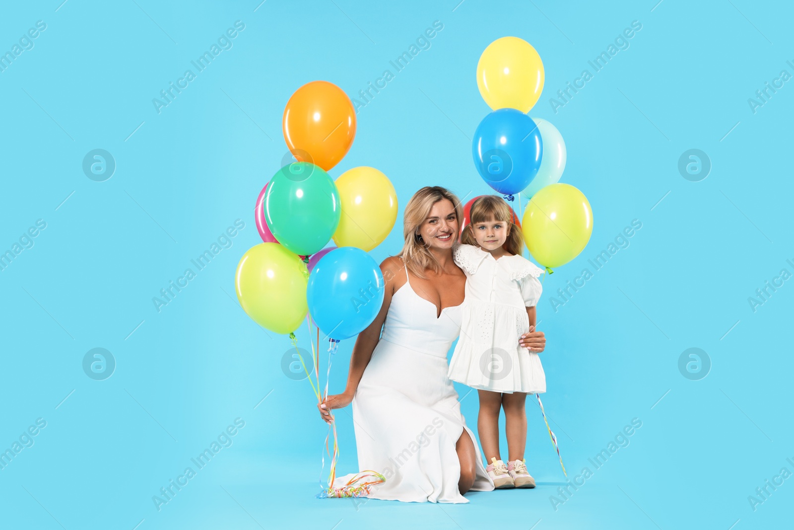 Photo of Happy mother and her little daughter with bunches of colorful balloons on light blue background