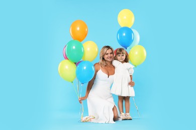 Photo of Happy mother and her little daughter with bunches of colorful balloons on light blue background