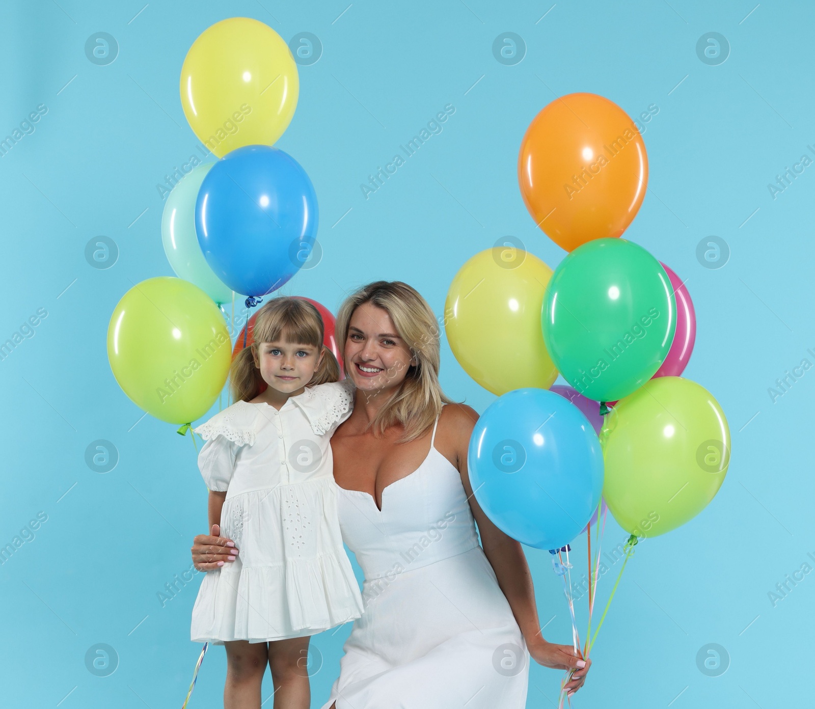 Happy mother and her little daughter with bunches of colorful balloons on light blue background Photo of Happy mother and her little daughter with bunches of colorful balloons on light blue background