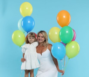 Photo of Happy mother and her little daughter with bunches of colorful balloons on light blue background