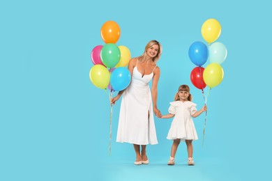 Photo of Happy mother and her little daughter with bunches of colorful balloons holding hands on light blue background