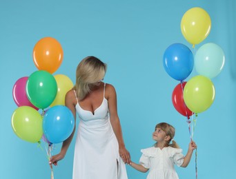 Photo of Mother and her little daughter with bunches of colorful balloons holding hands on light blue background