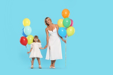 Photo of Happy mother and her little daughter with bunches of colorful balloons holding hands on light blue background