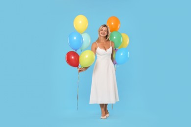 Photo of Smiling woman in dress with bunches of colorful balloons on light blue background