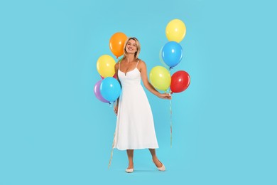 Photo of Smiling woman in dress with bunches of colorful balloons on light blue background