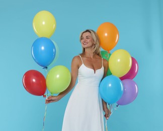 Photo of Smiling woman in dress with bunches of colorful balloons on light blue background