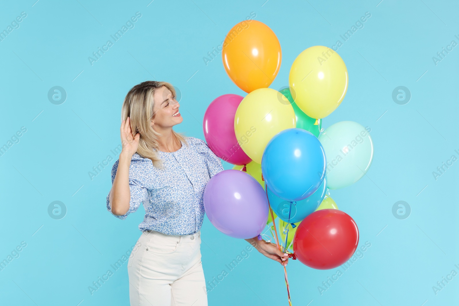 Photo of Smiling woman with bunch of colorful balloons on light blue background