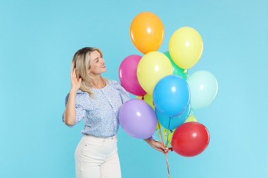 Photo of Smiling woman with bunch of colorful balloons on light blue background