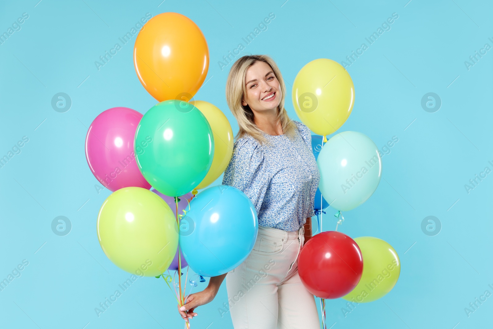 Photo of Smiling woman with bunches of colorful balloons on light blue background
