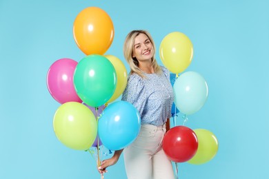 Photo of Smiling woman with bunches of colorful balloons on light blue background