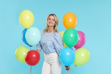 Photo of Smiling woman with bunches of colorful balloons on light blue background