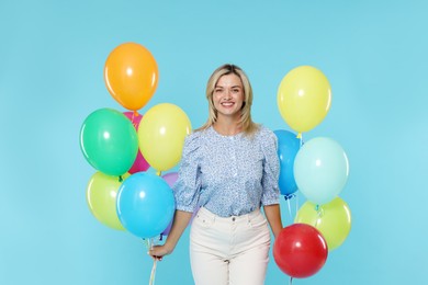 Photo of Smiling woman with bunches of colorful balloons on light blue background