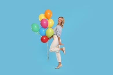 Photo of Smiling woman with bunch of colorful balloons on light blue background