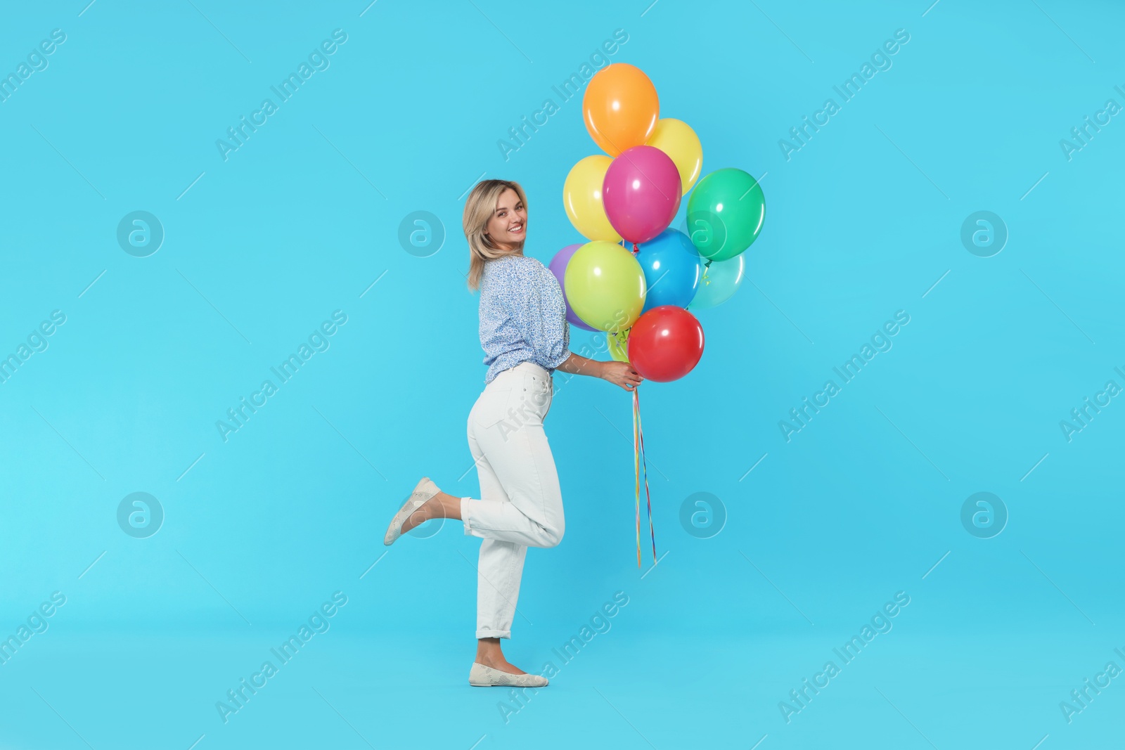Smiling woman with bunch of colorful balloons on light blue background Photo of Smiling woman with bunch of colorful balloons on light blue background