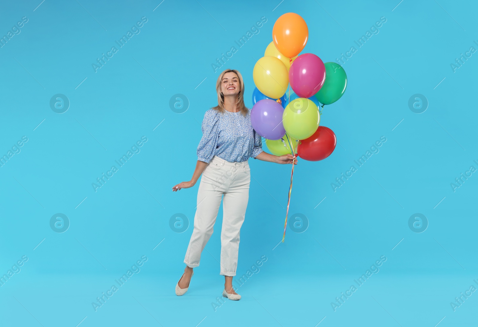 Smiling woman with bunch of colorful balloons on light blue background Photo of Smiling woman with bunch of colorful balloons on light blue background