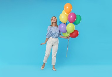 Photo of Smiling woman with bunch of colorful balloons on light blue background