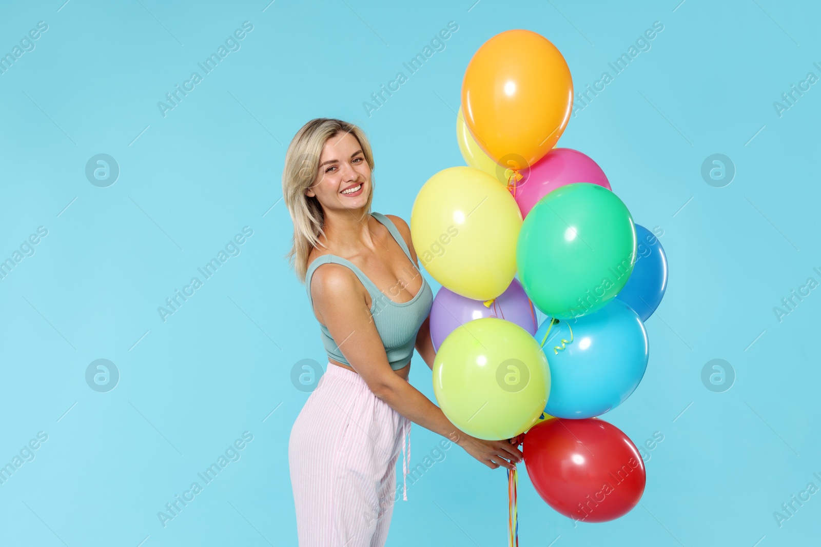Photo of Smiling woman with bunch of colorful balloons on light blue background
