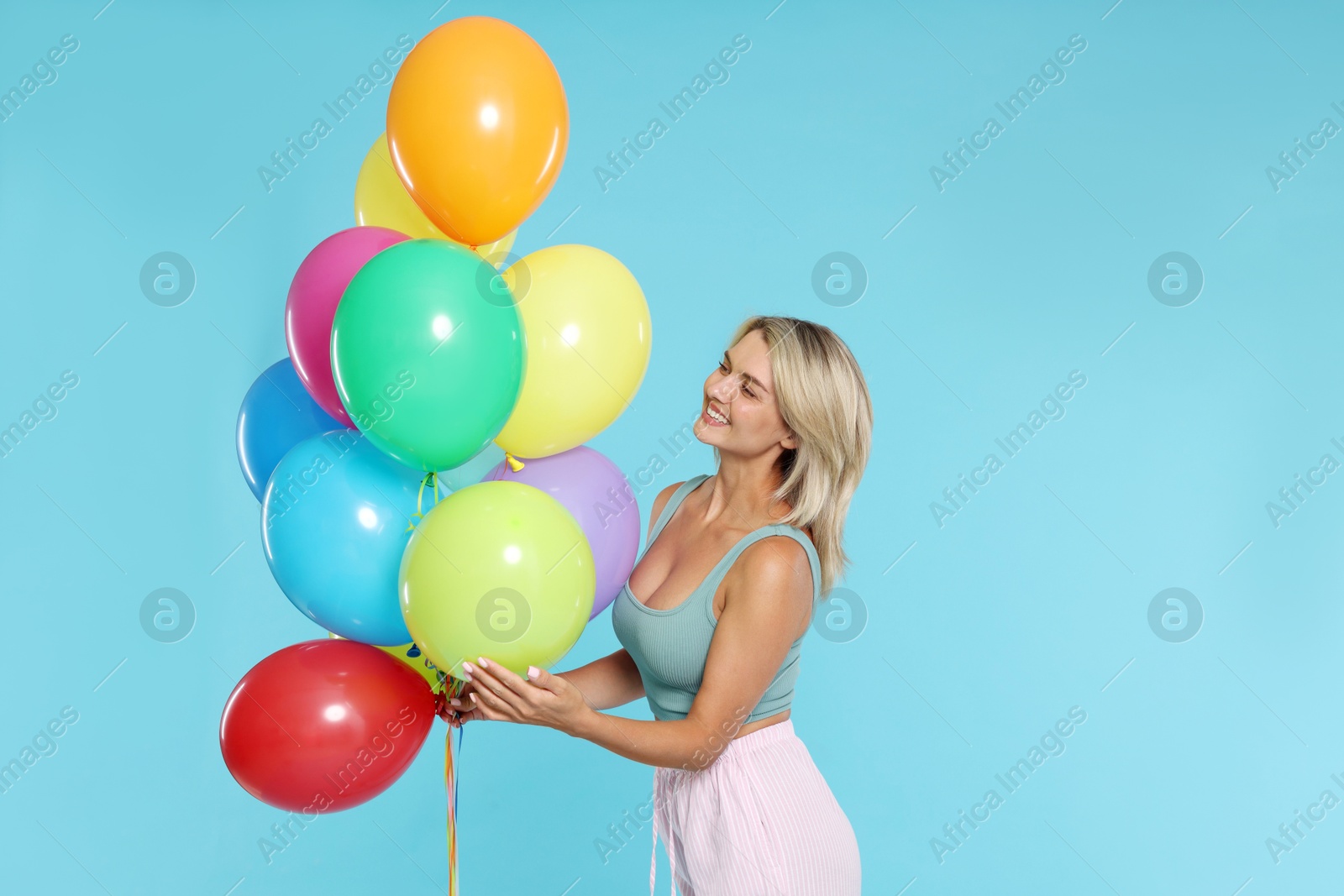 Photo of Smiling woman with bunch of colorful balloons on light blue background