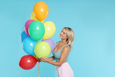 Photo of Smiling woman with bunch of colorful balloons on light blue background