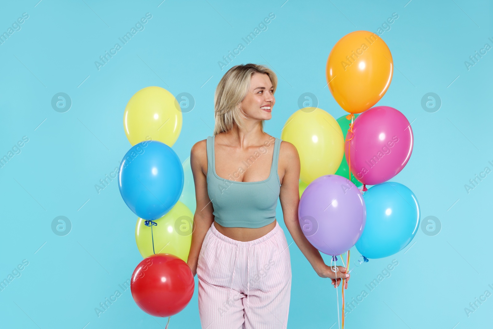 Photo of Smiling woman with bunches of colorful balloons on light blue background