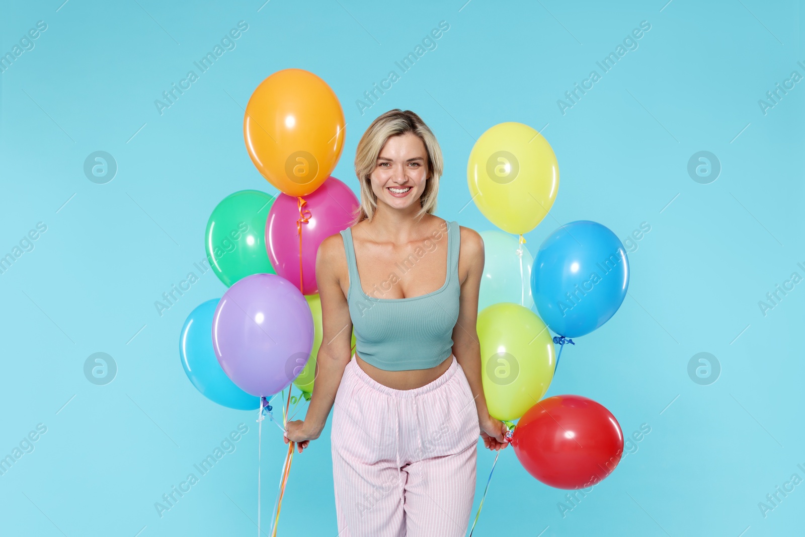 Photo of Smiling woman with bunches of colorful balloons on light blue background