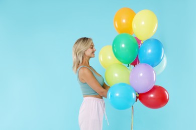 Photo of Smiling woman with bunch of colorful balloons on light blue background