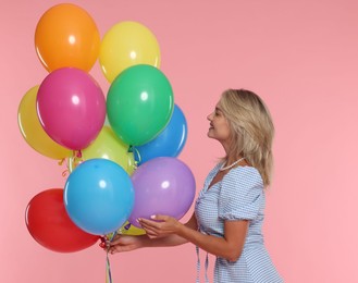 Photo of Smiling woman with bunch of colorful balloons on pink background