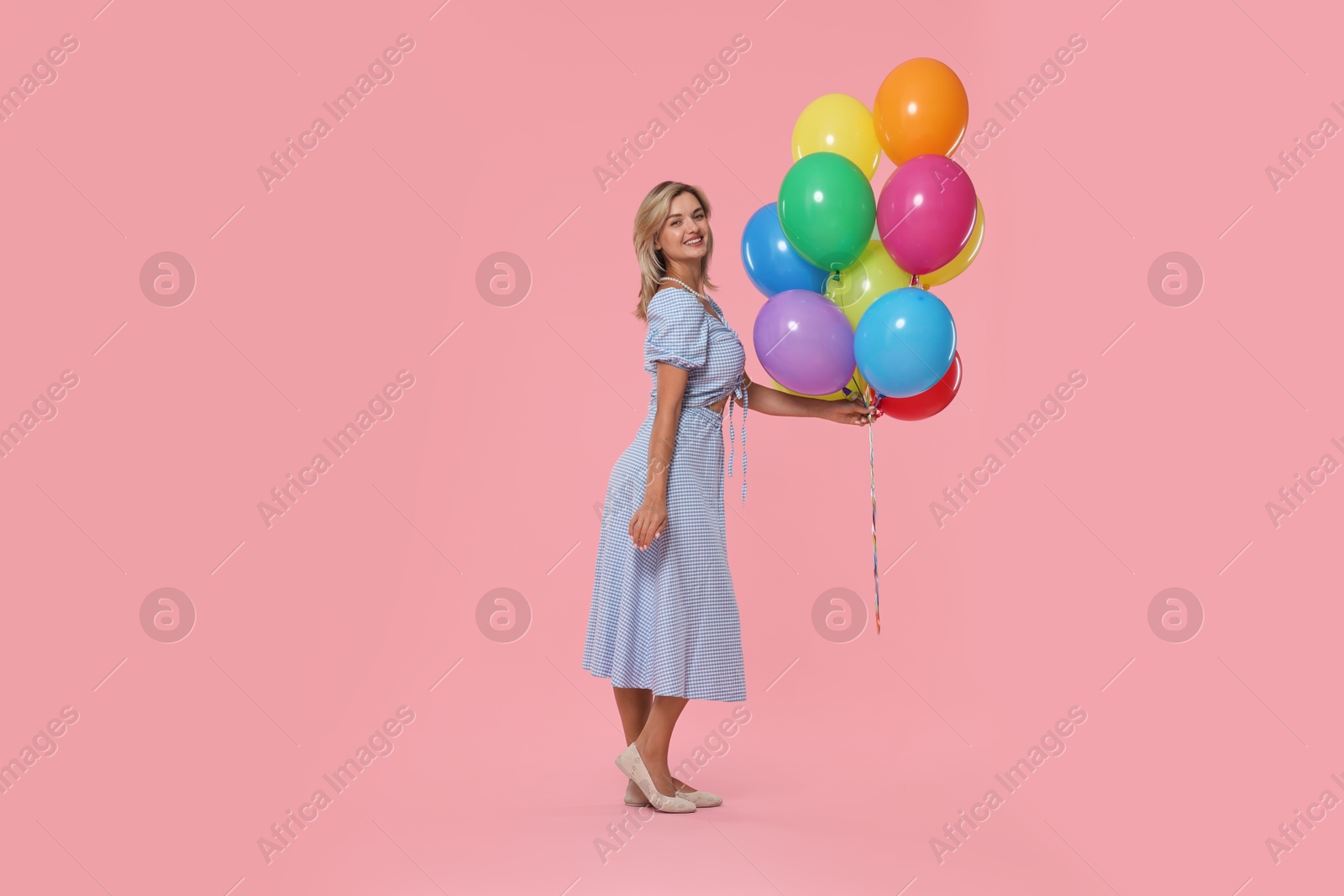 Smiling woman with bunch of colorful balloons on pink background Photo of Smiling woman with bunch of colorful balloons on pink background