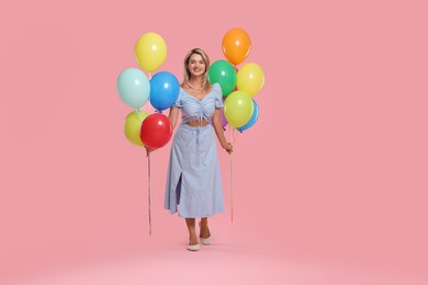 Photo of Smiling woman with bunches of colorful balloons on pink background