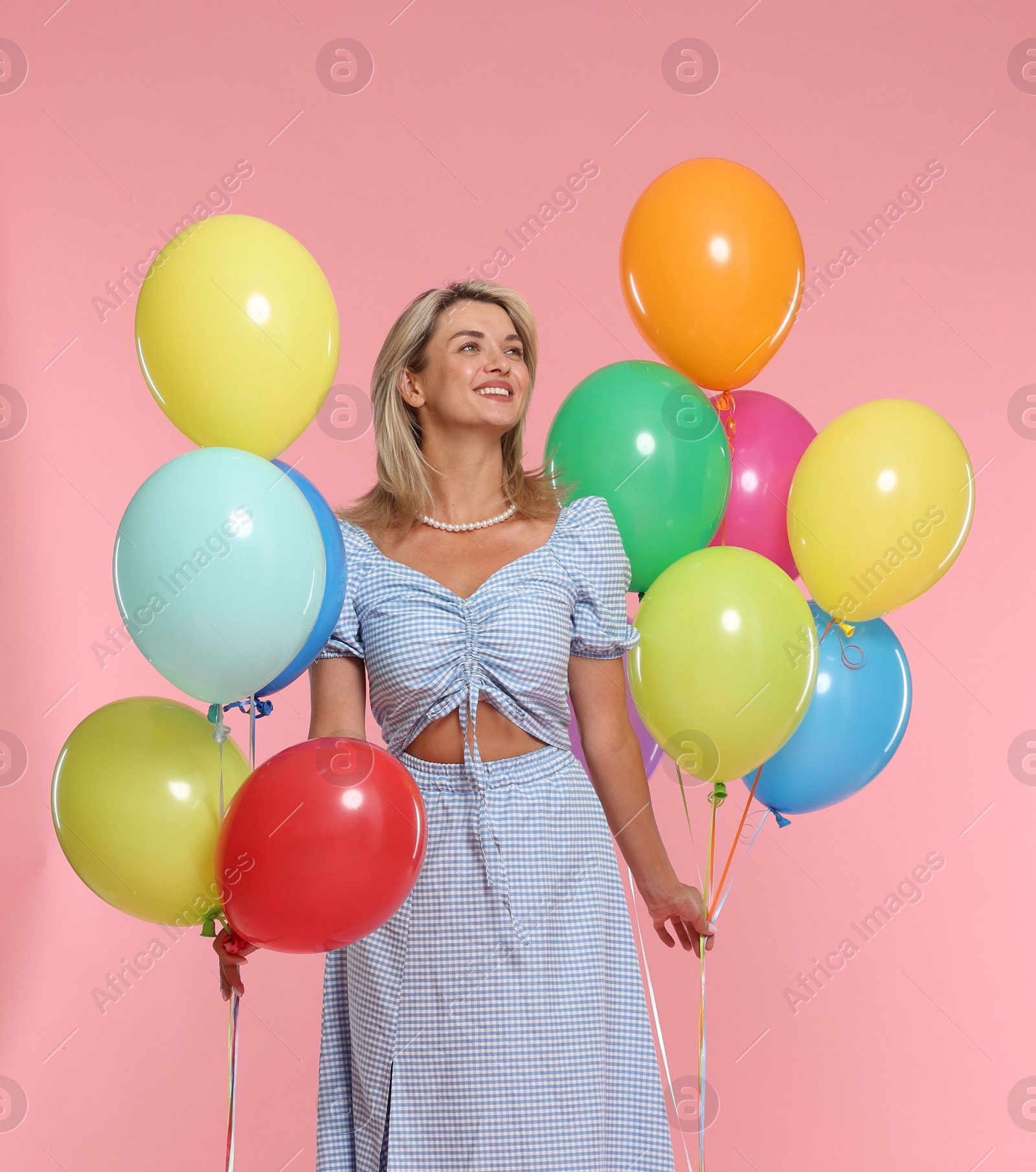 Photo of Smiling woman with bunches of colorful balloons on pink background