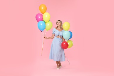 Photo of Smiling woman with bunches of colorful balloons on pink background