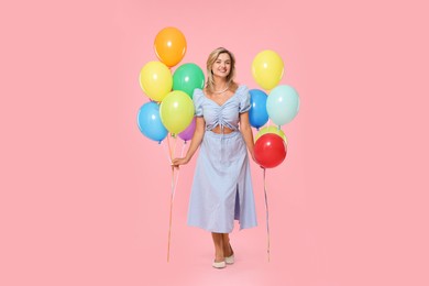 Photo of Smiling woman with bunches of colorful balloons on pink background