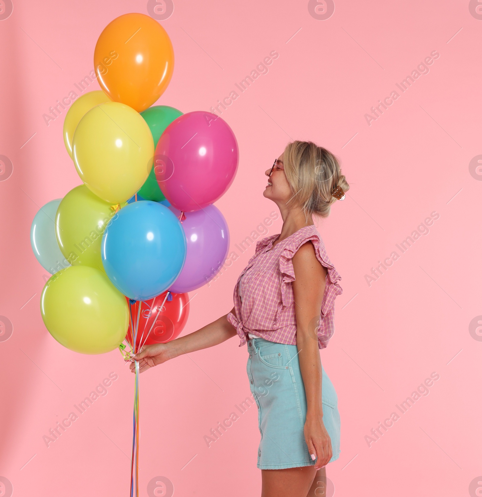 Photo of Smiling woman in sunglasses with bunch of colorful balloons on pink background