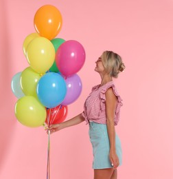 Photo of Smiling woman in sunglasses with bunch of colorful balloons on pink background
