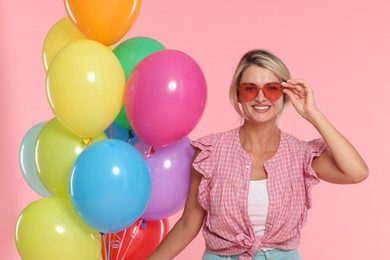 Photo of Smiling woman in sunglasses with bunch of colorful balloons on pink background