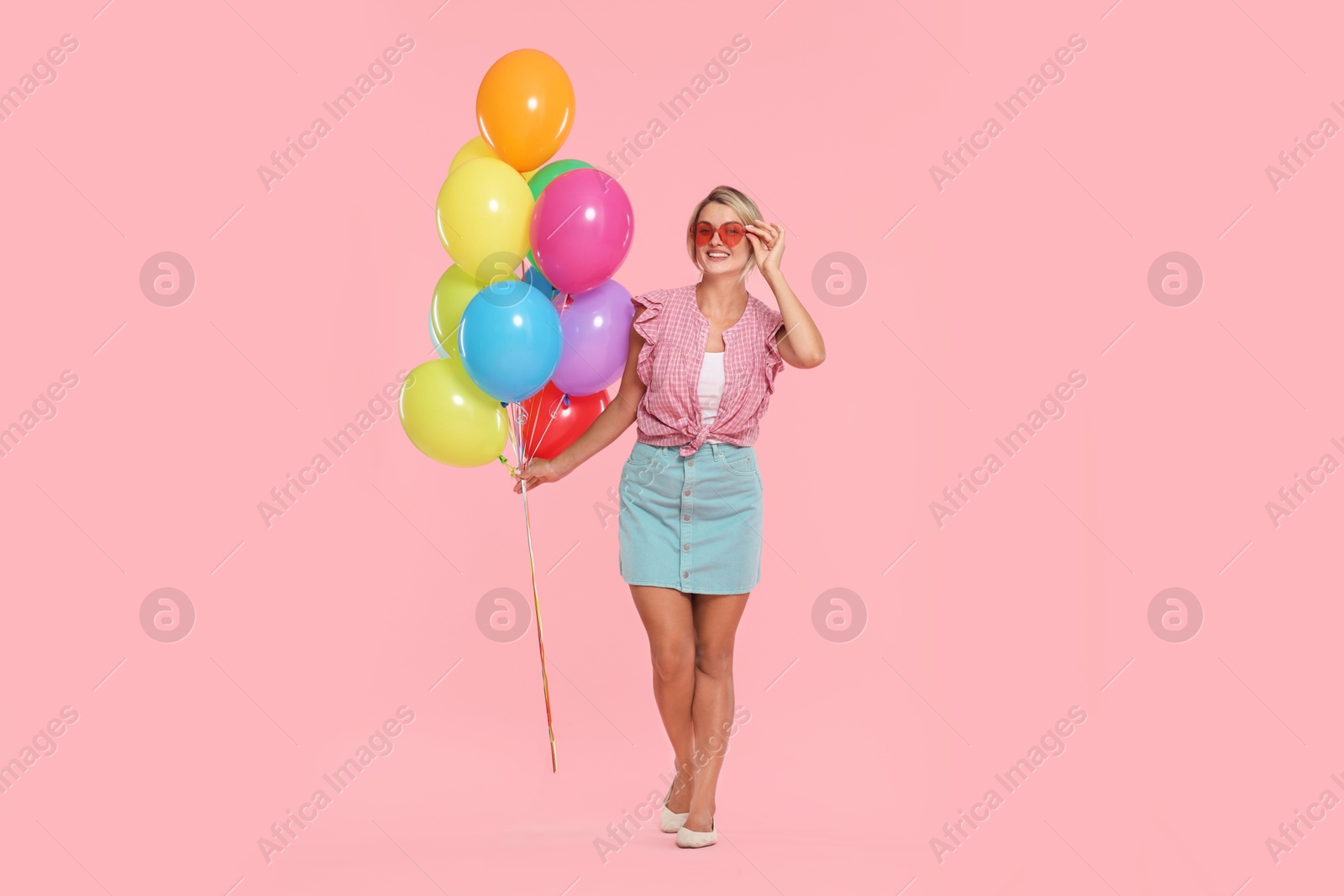 Smiling woman in sunglasses with bunch of colorful balloons on pink background Photo of Smiling woman in sunglasses with bunch of colorful balloons on pink background