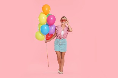 Photo of Smiling woman in sunglasses with bunch of colorful balloons on pink background